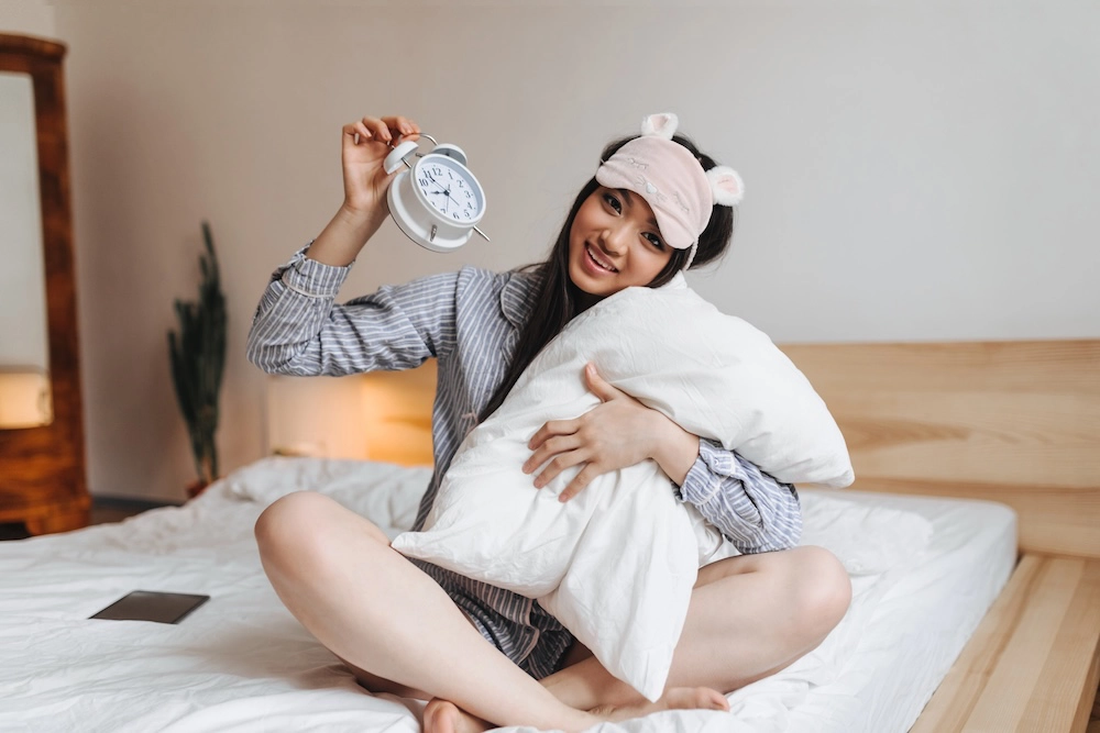 Woman sitting on a bed and hugging a pillow in a sleep-friendly bedroom